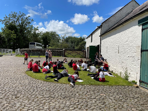 A group of children sitting doing work on the grass on a sunny day